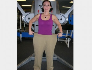 a front view photo of smiling female transformation client wearing her former pants to show how much weight she has lost