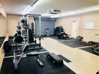 photo 6 of the back room of FIIT by Jason Smith facility showing rebok deck, bicep curl machine, leg curl machine, medicine ball rack with medicine balls, squat rack and weight plates for resistance training, cardiovascular training and functional training in Phoenix, AZ